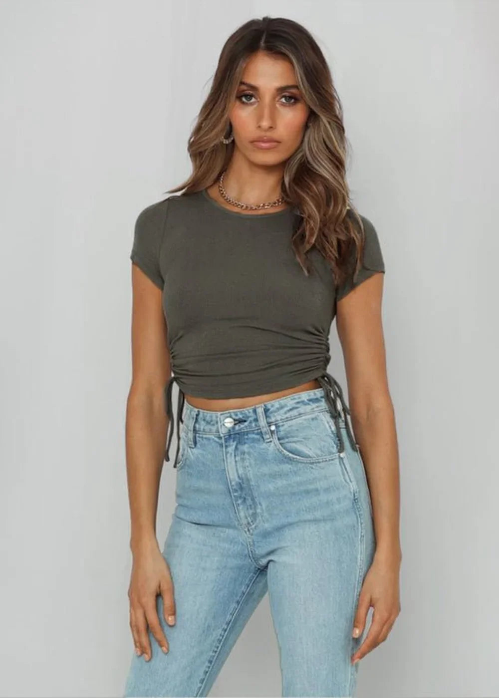 Olive green ruched crop top with drawstring details and light wash denim jeans on a model.