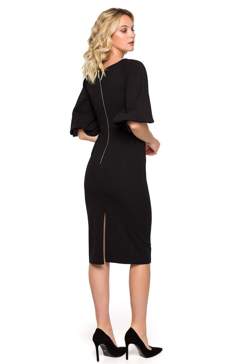 Black knee-length dress with dramatic bell sleeves, a back zipper, and a side slit, worn with black heels.