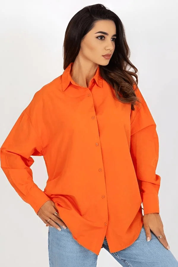 Woman in loose-fit, bright orange, long-sleeved button-up shirt and light blue jeans.