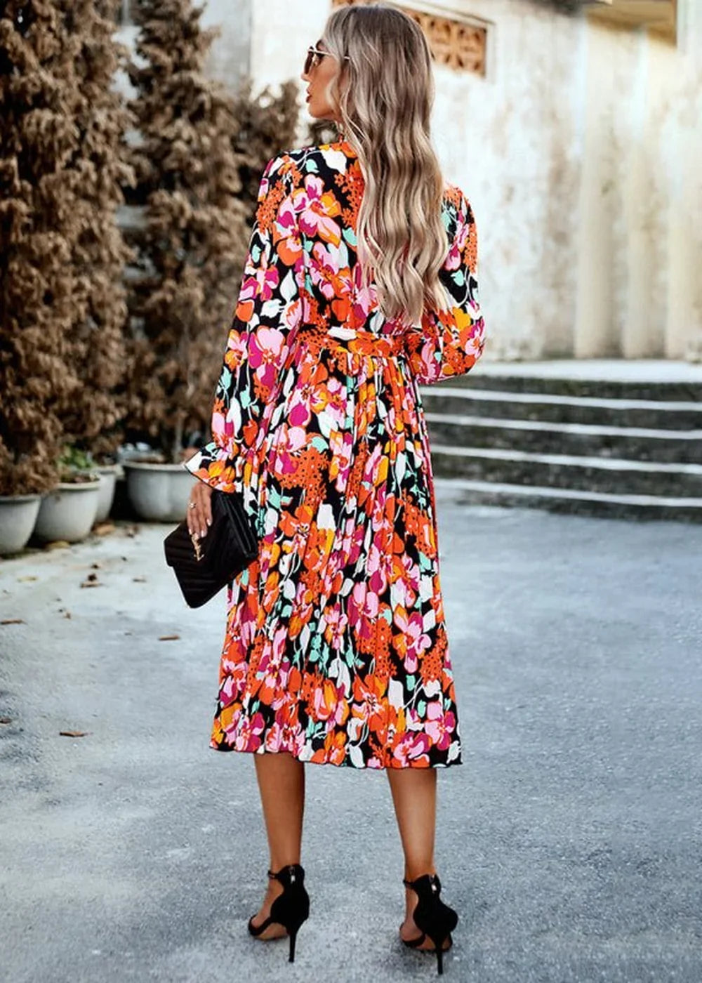 Back view of a woman wearing a vibrant floral print midi dress with black heels and a black clutch.