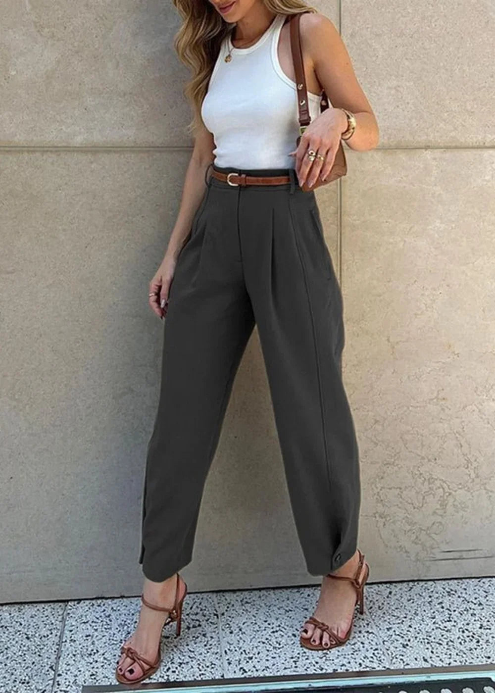 Dark gray wide-leg pants with pleats and ankle button details, paired with a white tank top and brown heels on a model.