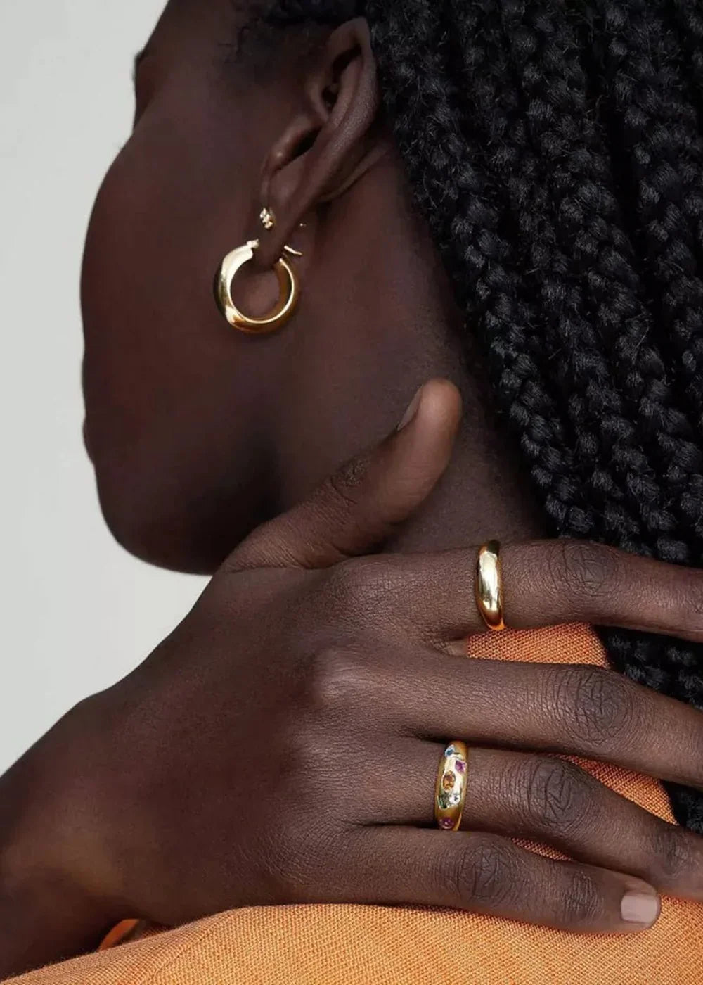 Close-up of a dark-skinned hand adorned with gold hoop earrings and two gold rings, one with colorful zircon stones.