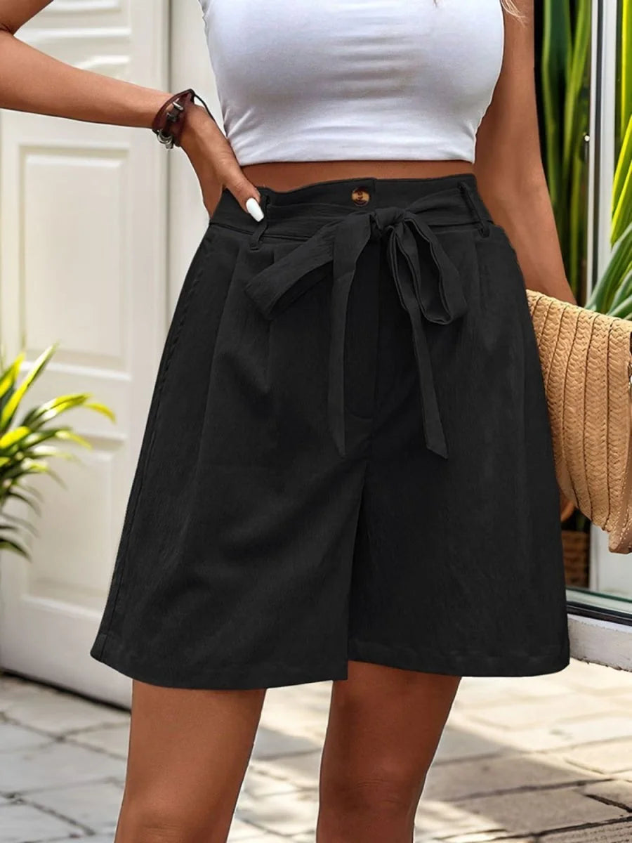 Black textured paperbag waist shorts with a self-tie belt, shown on a model.