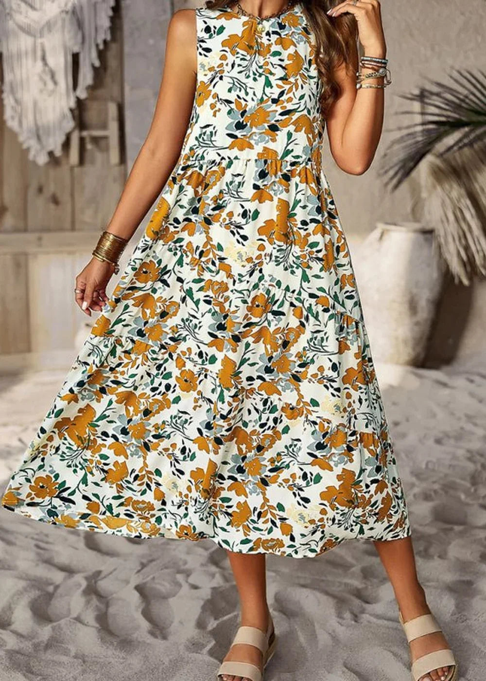 White sleeveless midi dress with a yellow and green floral print, tiered skirt, and gold bracelets.