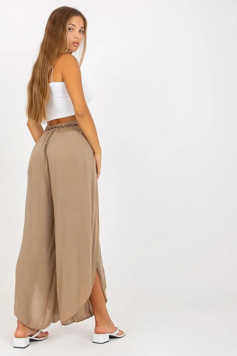 Woman from the back wearing loose, beige, flowing pants with side slits and a white crop top.