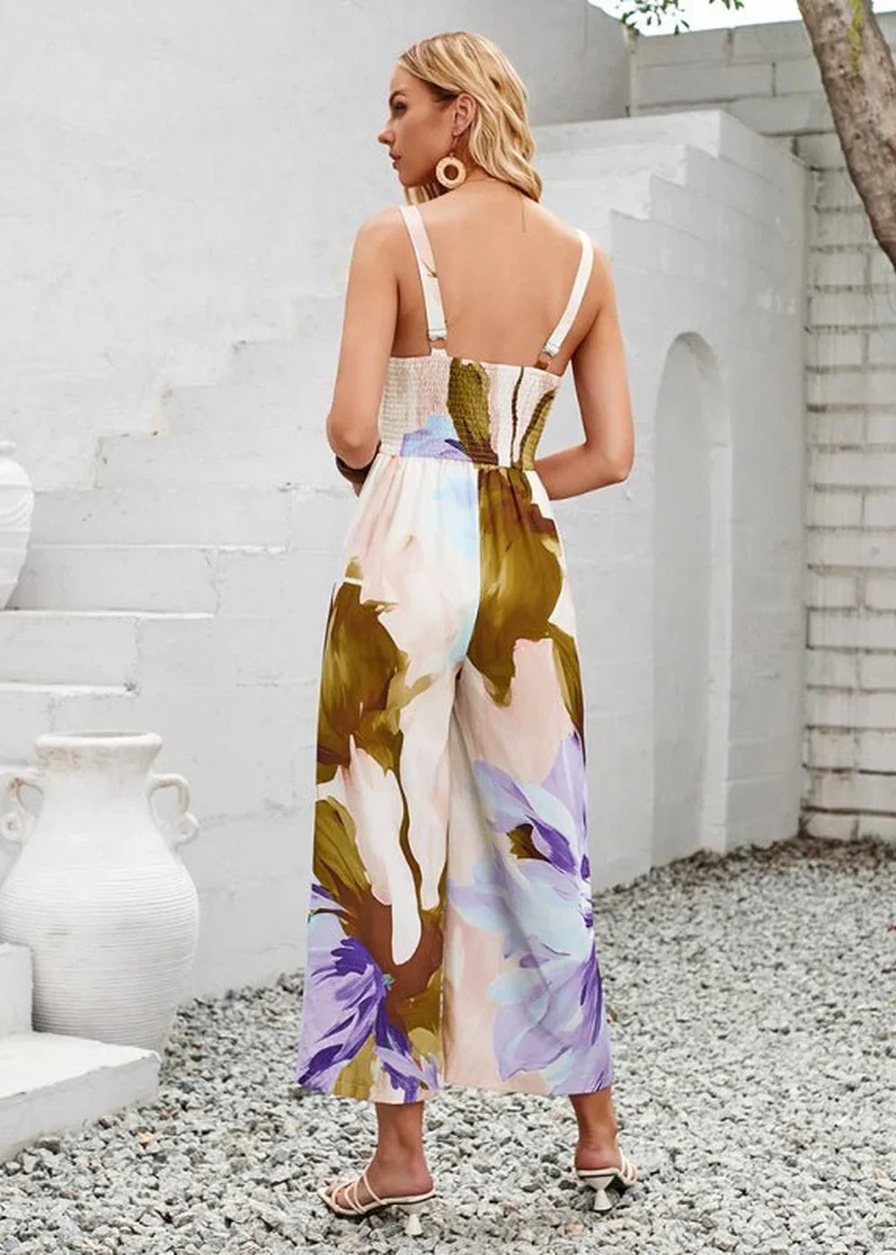 Woman in a flowing wide-leg jumpsuit with a bold abstract floral print in purple, green, and blush pink.