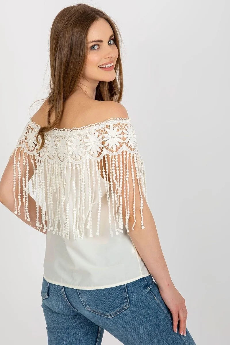 Off-the-shoulder white lace top with fringe trim over a white camisole, worn with blue jeans.