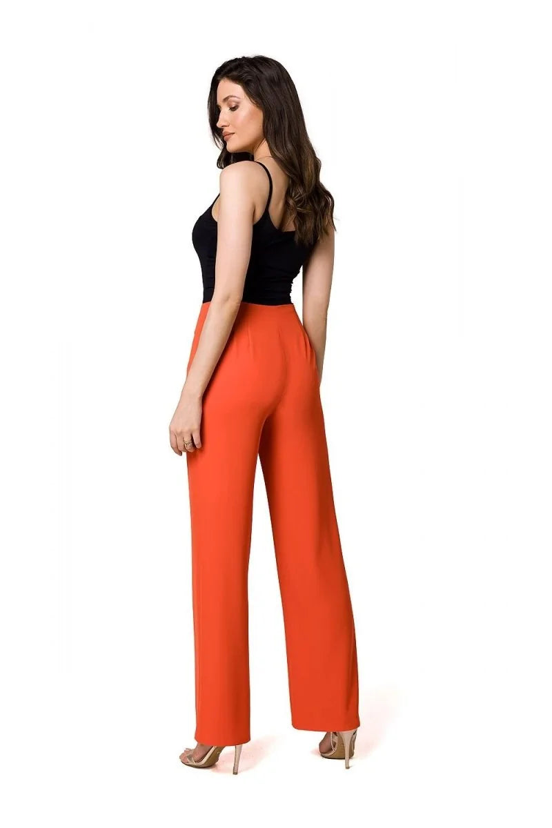 Woman from behind wearing bright orange wide-leg pants and a black tank top, with gold heels.