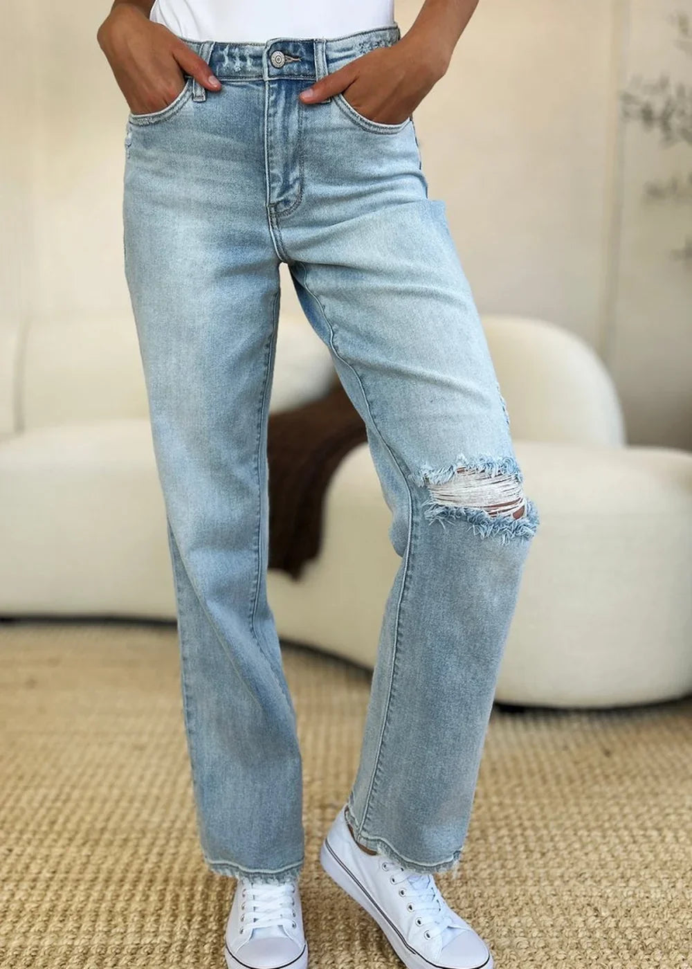 Light blue distressed denim jeans with frayed hem and ripped knee detail on model.