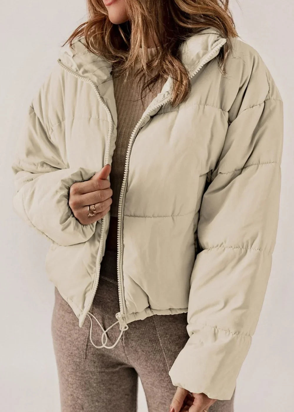 Cream puffer jacket with zipper closure, ribbed texture, and drawstring waist on model.