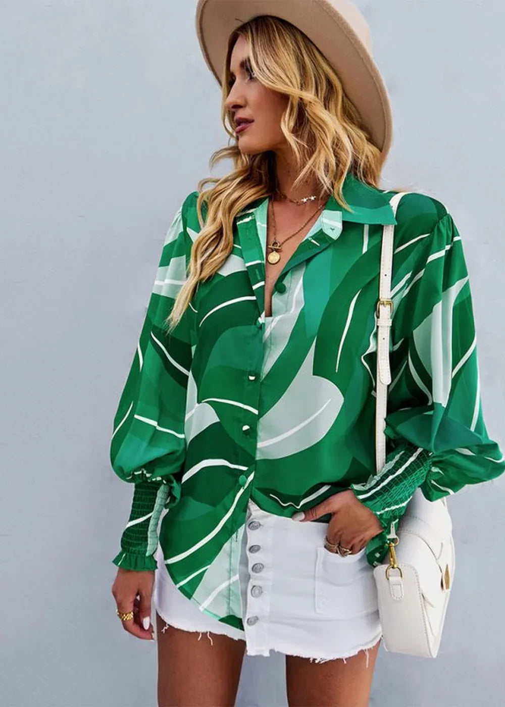 Woman in a green abstract leaf print blouse with puffed sleeves and a white denim skirt.