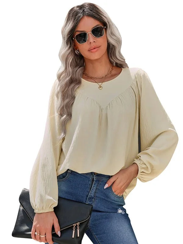 Cream long-sleeve peasant top with gathered neckline and elastic cuffs, paired with blue jeans.