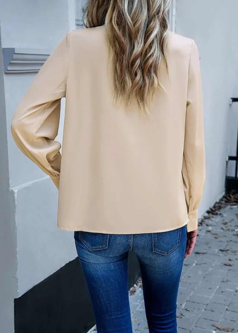 Back view of a woman wearing a tan long-sleeved polyester top and dark wash skinny jeans.