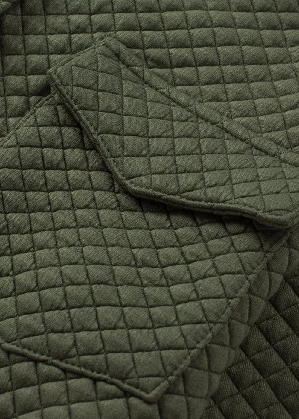 Close-up of olive green quilted fabric with diamond pattern and pocket details.