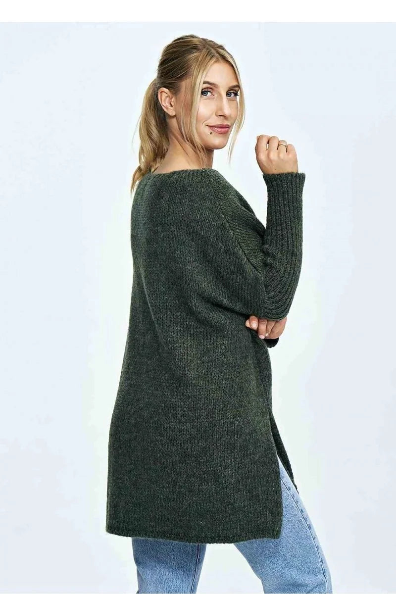 Woman in a loose-fit, dark green knit sweater with side slits, paired with light blue jeans.