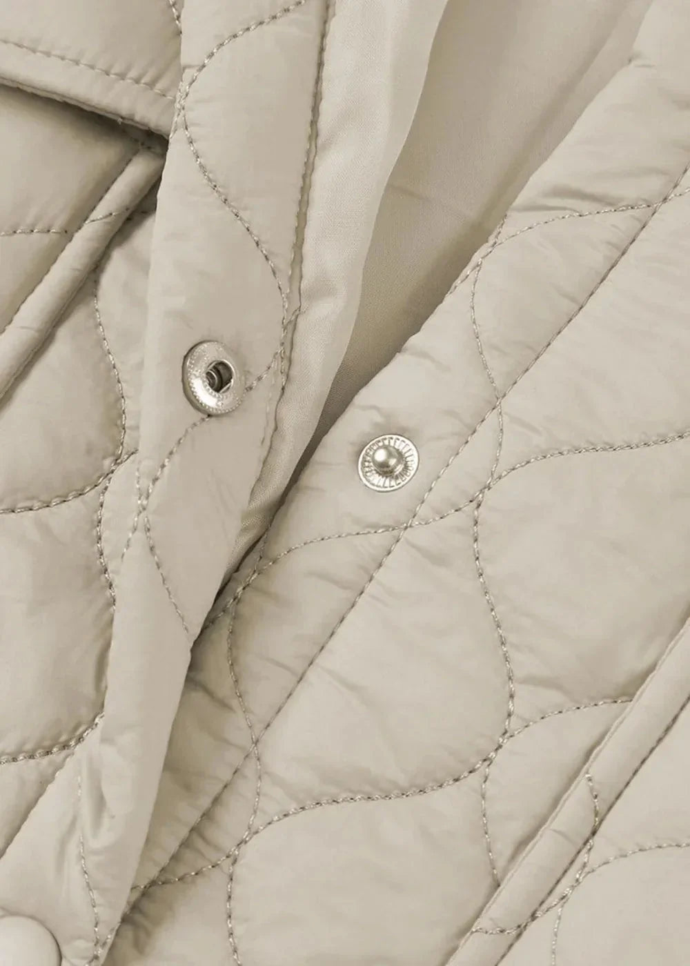 Close-up of a light beige quilted jacket with silver snap closures and diamond stitching.