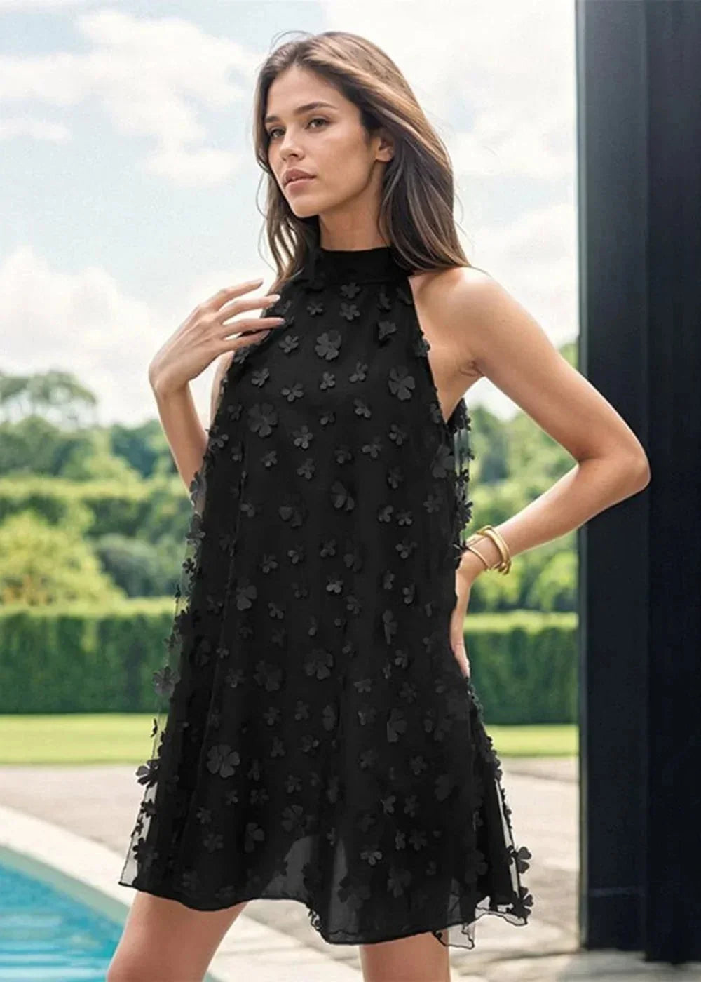Black floral applique halter dress on model with gold bracelet.