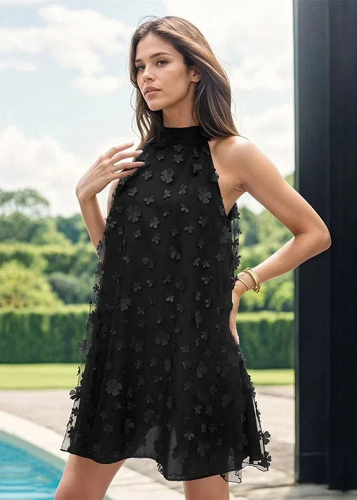 Black floral applique halter dress on model with gold bracelet.