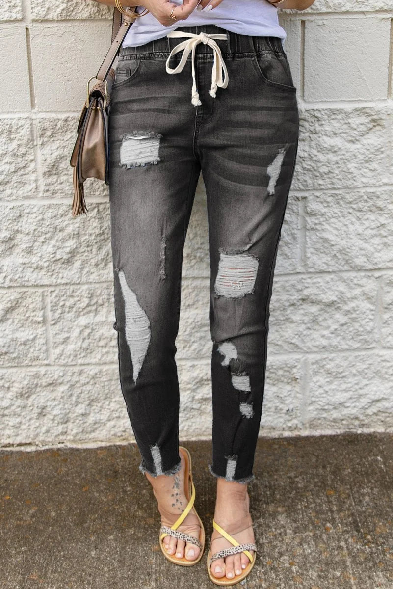 Distressed charcoal denim joggers with frayed hems and drawstring waist.