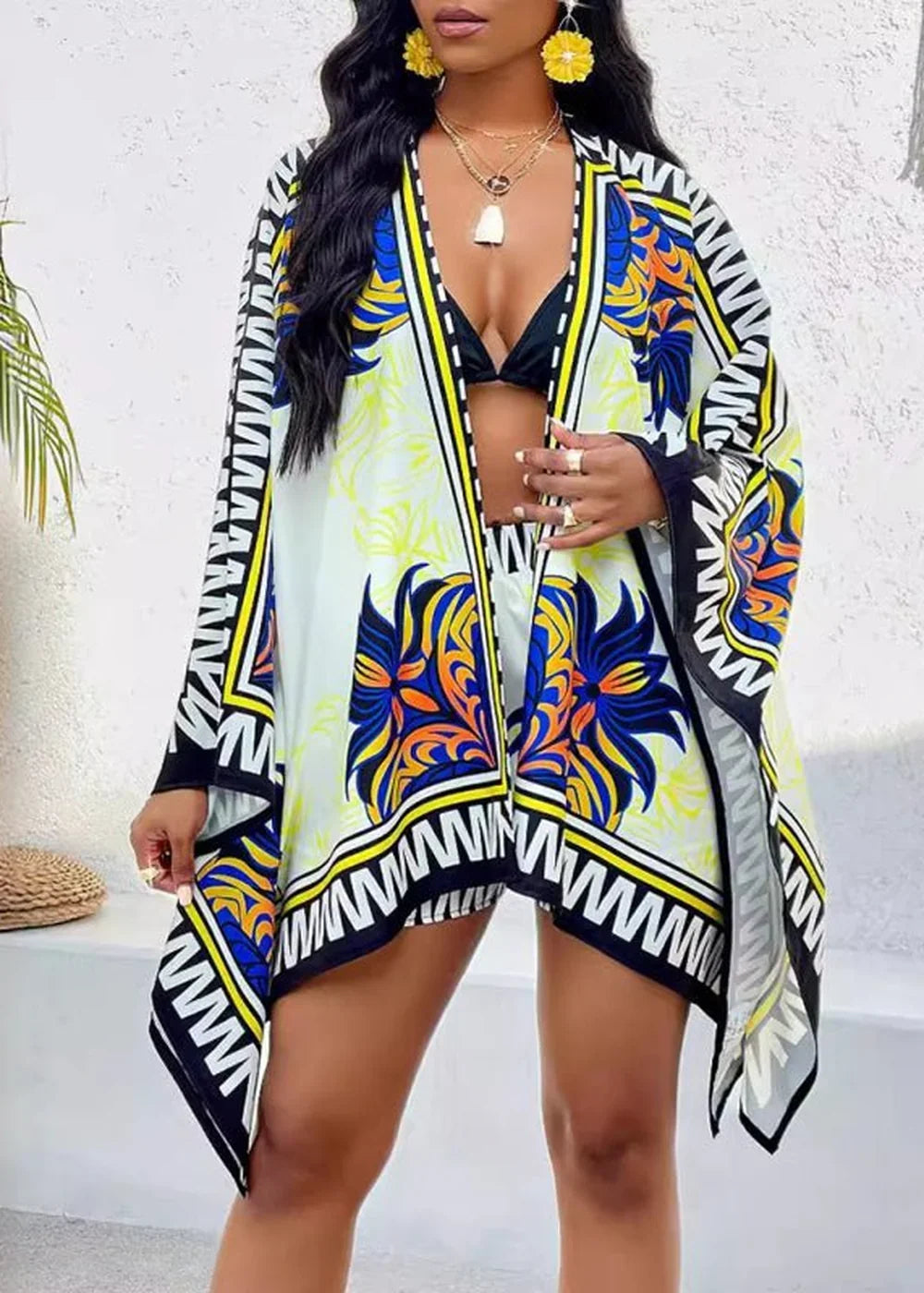 Woman wearing a flowing kimono with a vibrant blue, orange, and yellow floral print over a black bikini.