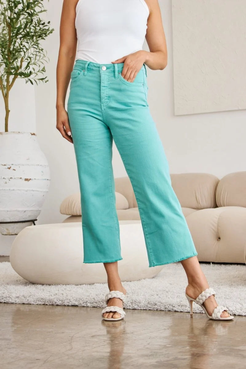 Cropped, turquoise denim jeans with a frayed hem and moderate stretch, shown on a model.