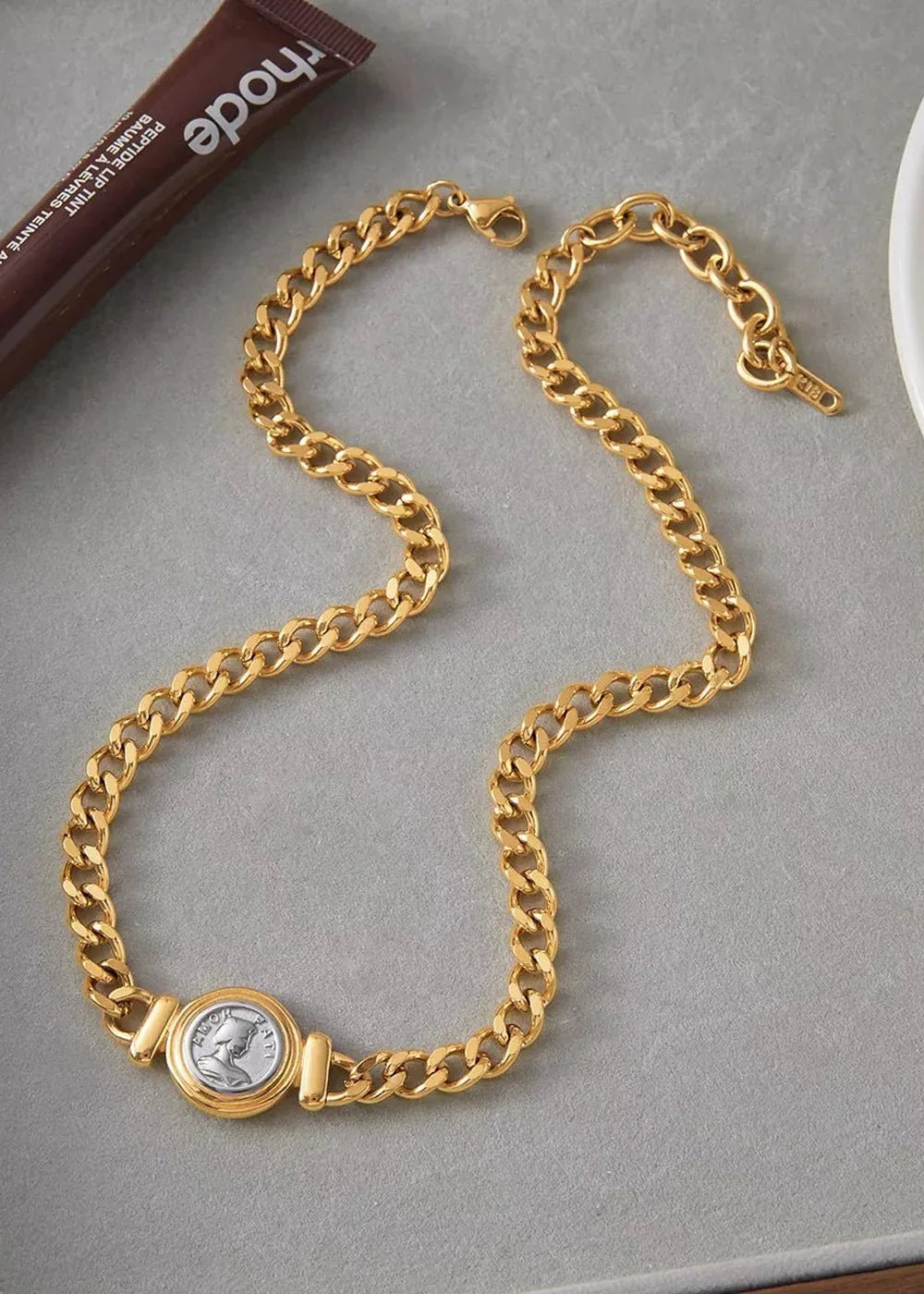 Gold-plated cuban link necklace with a silver coin pendant, on a grey background.