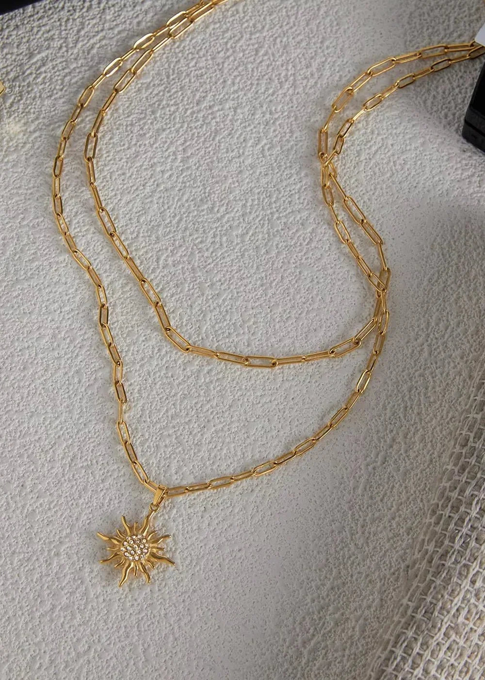 Gold layered chain necklace with a sunburst pendant adorned with rhinestones.