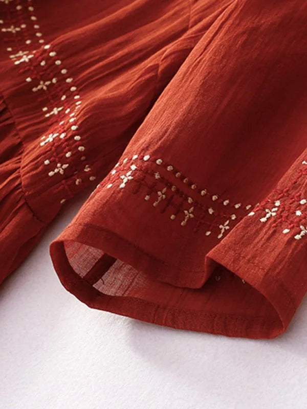 Close-up of a rust-colored linen-blend dress with embroidered details on the sleeves and bodice.