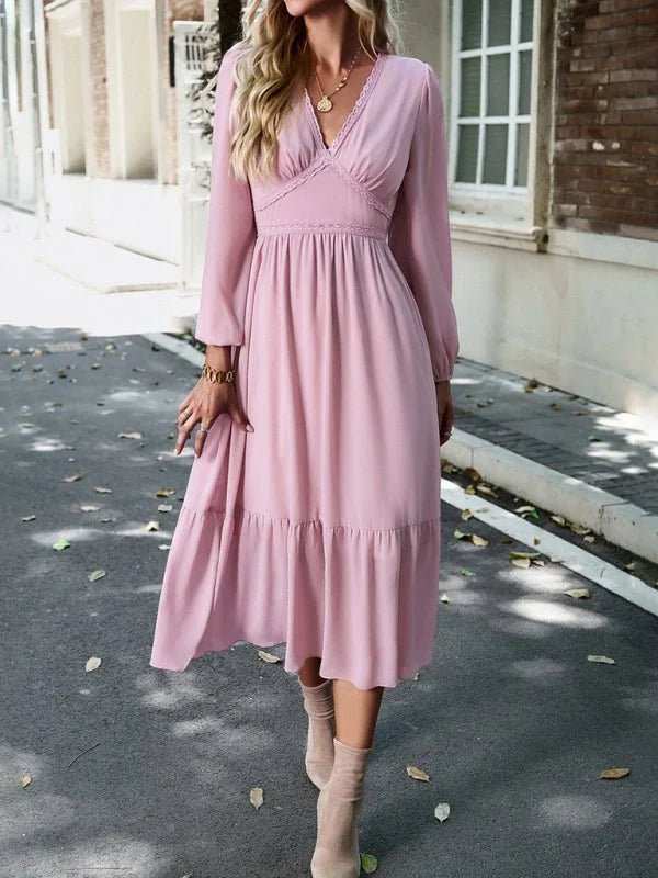 A woman in a flowy pink V-neck midi dress with lace trim and long sleeves.