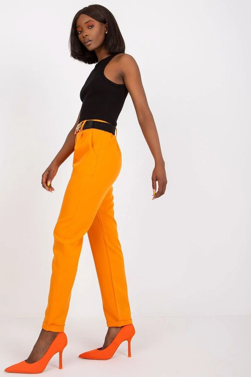 Woman wearing bright orange high-waisted trousers with a black belt and matching pointed-toe heels.
