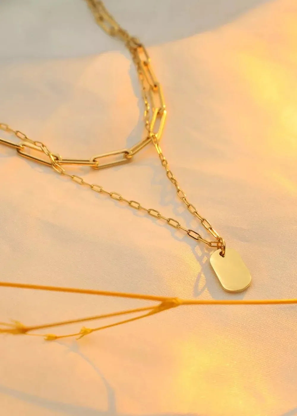 Two layered gold-plated stainless steel necklaces with paperclip chain and a tag pendant.