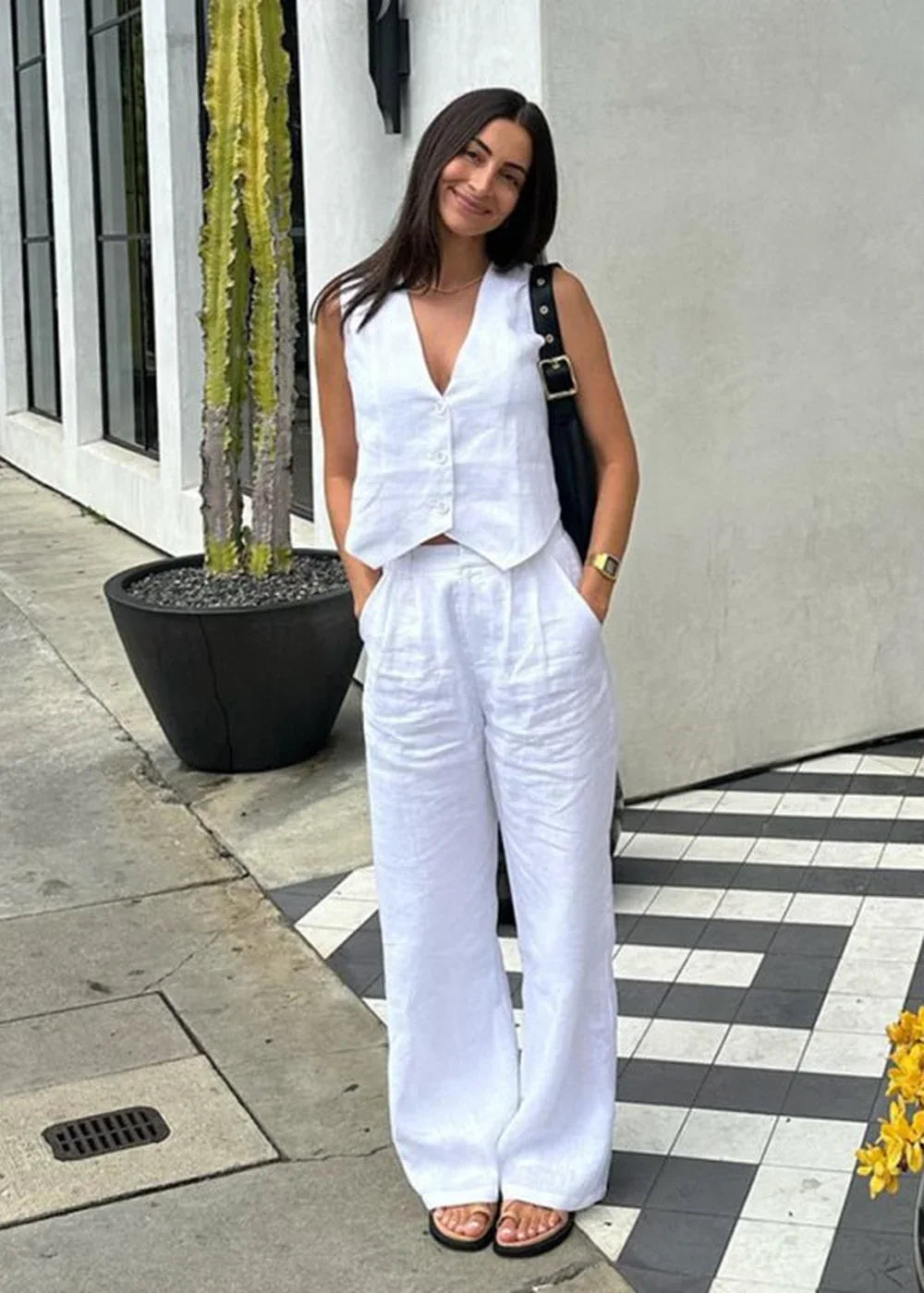 Woman in a white linen vest and wide-leg pants, standing with hands in pockets.