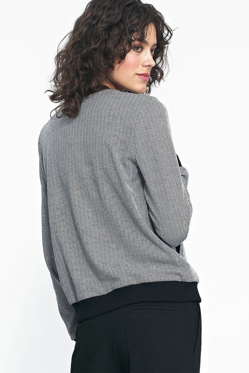 Woman from the back wearing a loose-cut, grey and black herringbone patterned jacket with a black ribbed hem.