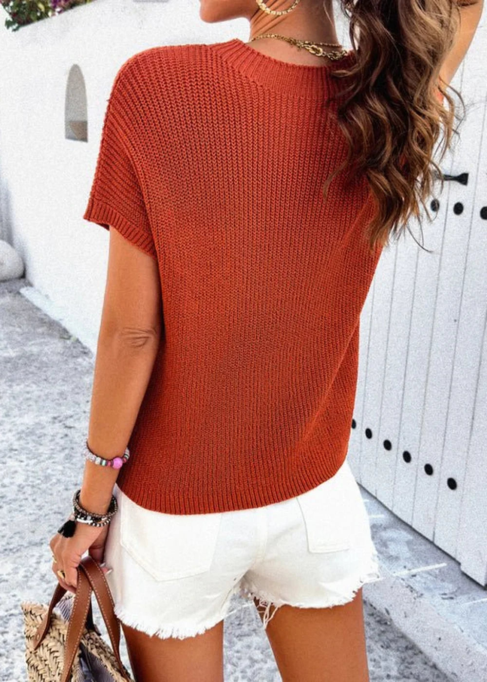 Back view of a rust-orange knit top with short sleeves and white frayed denim shorts.