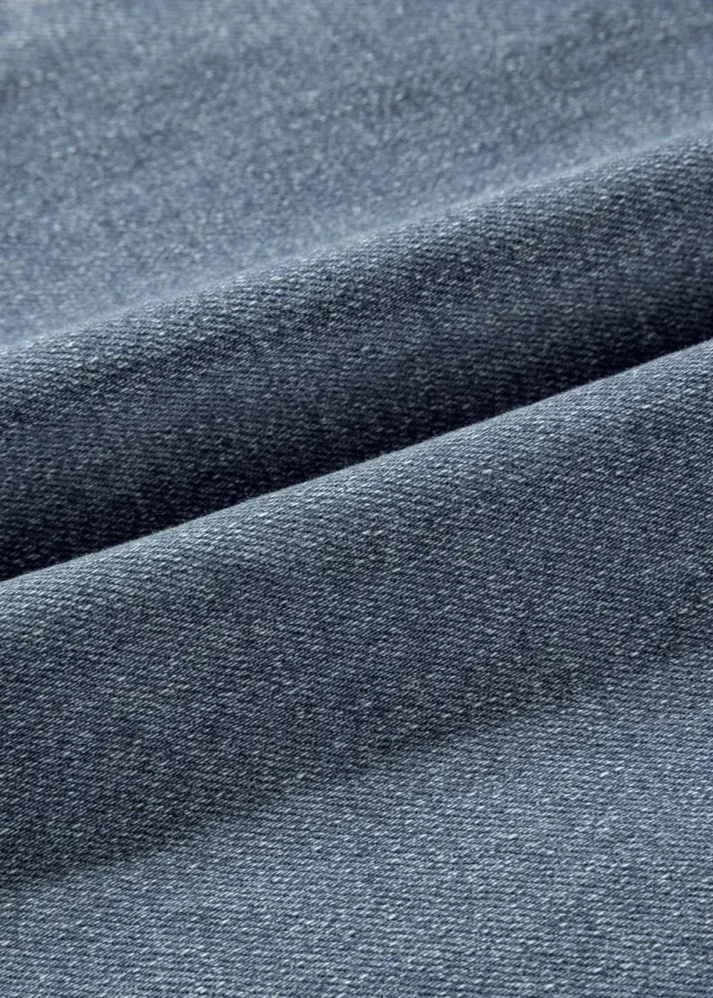 Close-up of dark blue denim fabric with a subtle texture, showing folds and seams.