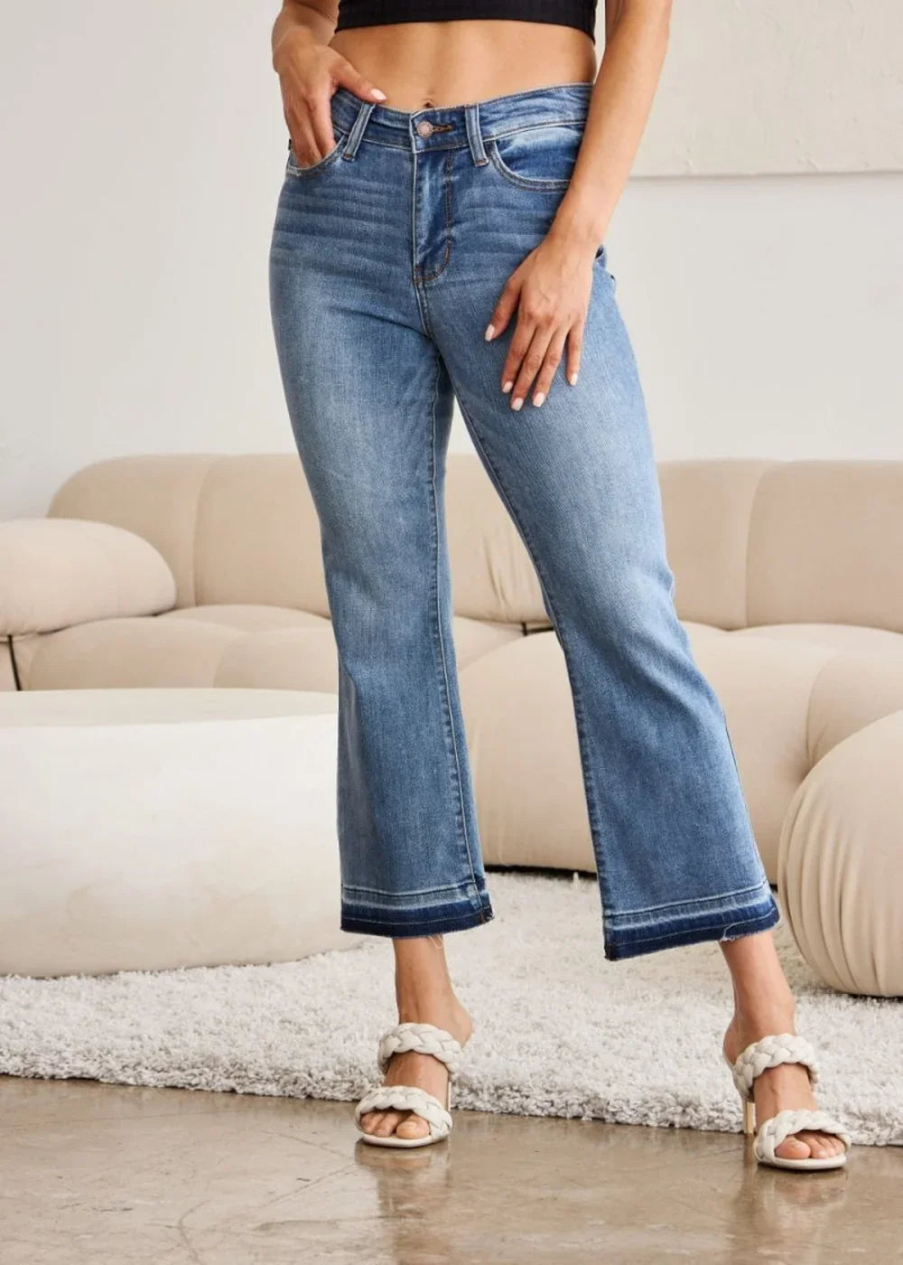 Medium wash distressed denim flare jeans with frayed hem, on model.