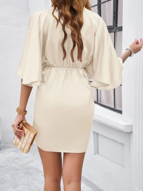 Cream flowy-sleeve mini dress with cinched waist, held gold patterned clutch, on model.