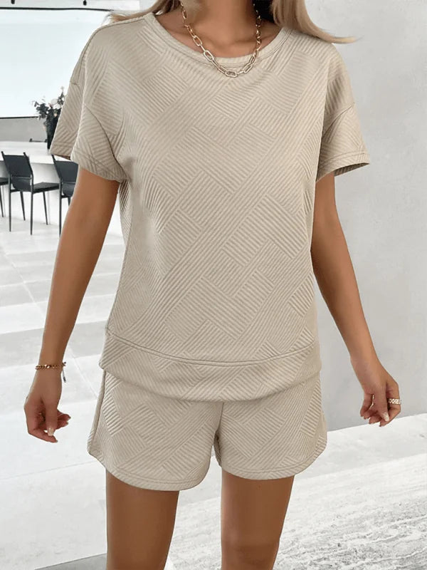 Beige textured short suit with a subtle geometric pattern and a gold chain necklace.