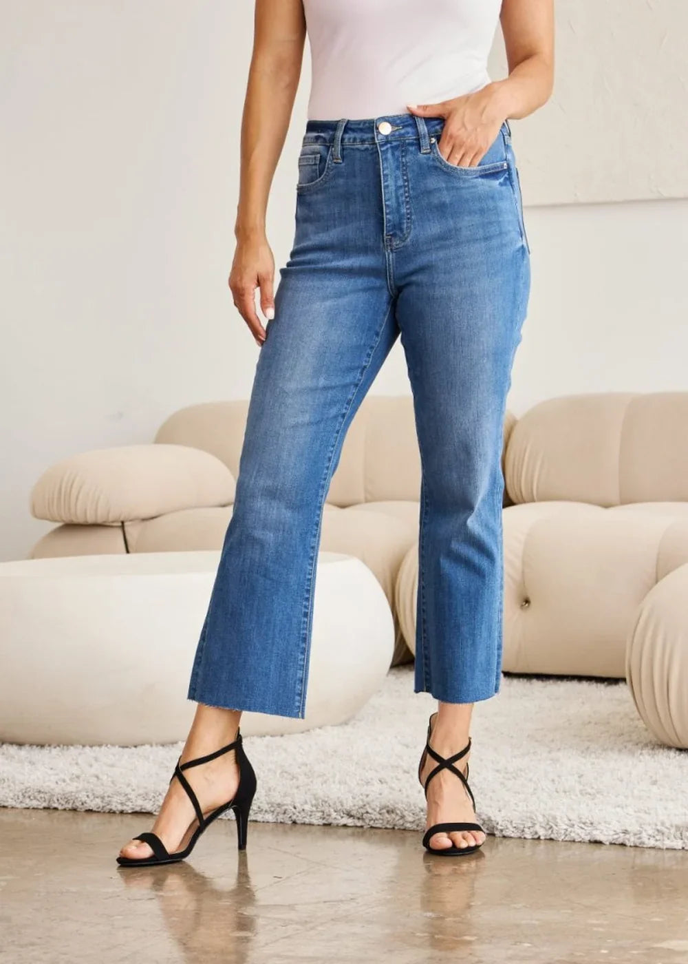 Medium wash denim jeans with a frayed hem and a flared leg, worn with black strappy heels.