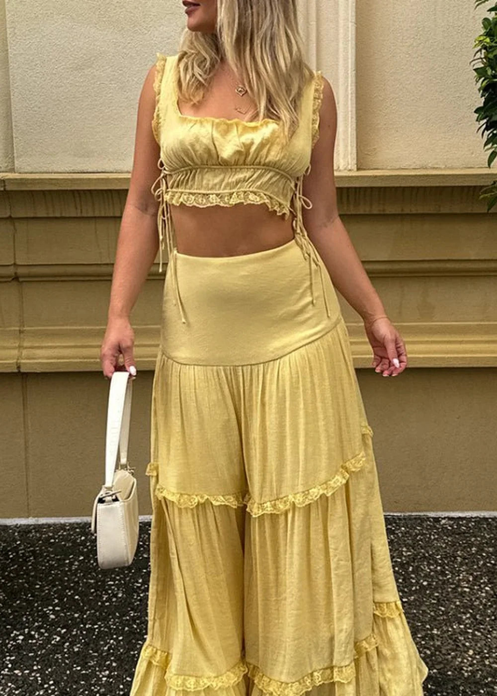 Yellow tiered maxi skirt with lace trim and matching crop top, held by a white handbag.