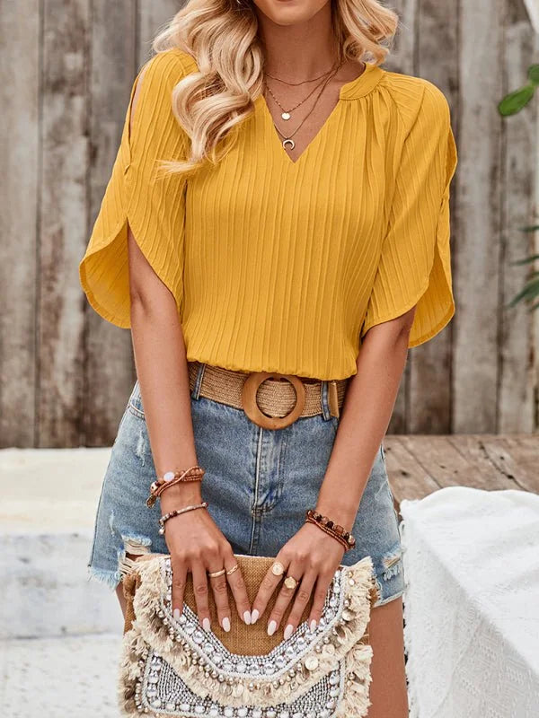 Yellow pleated V-neck top with split sleeves, paired with distressed denim shorts and boho clutch.