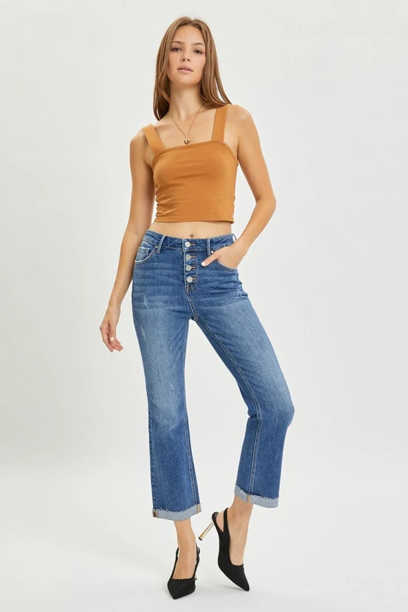 Woman in high-waisted, distressed blue denim jeans with a cuffed hem and four-button fly.