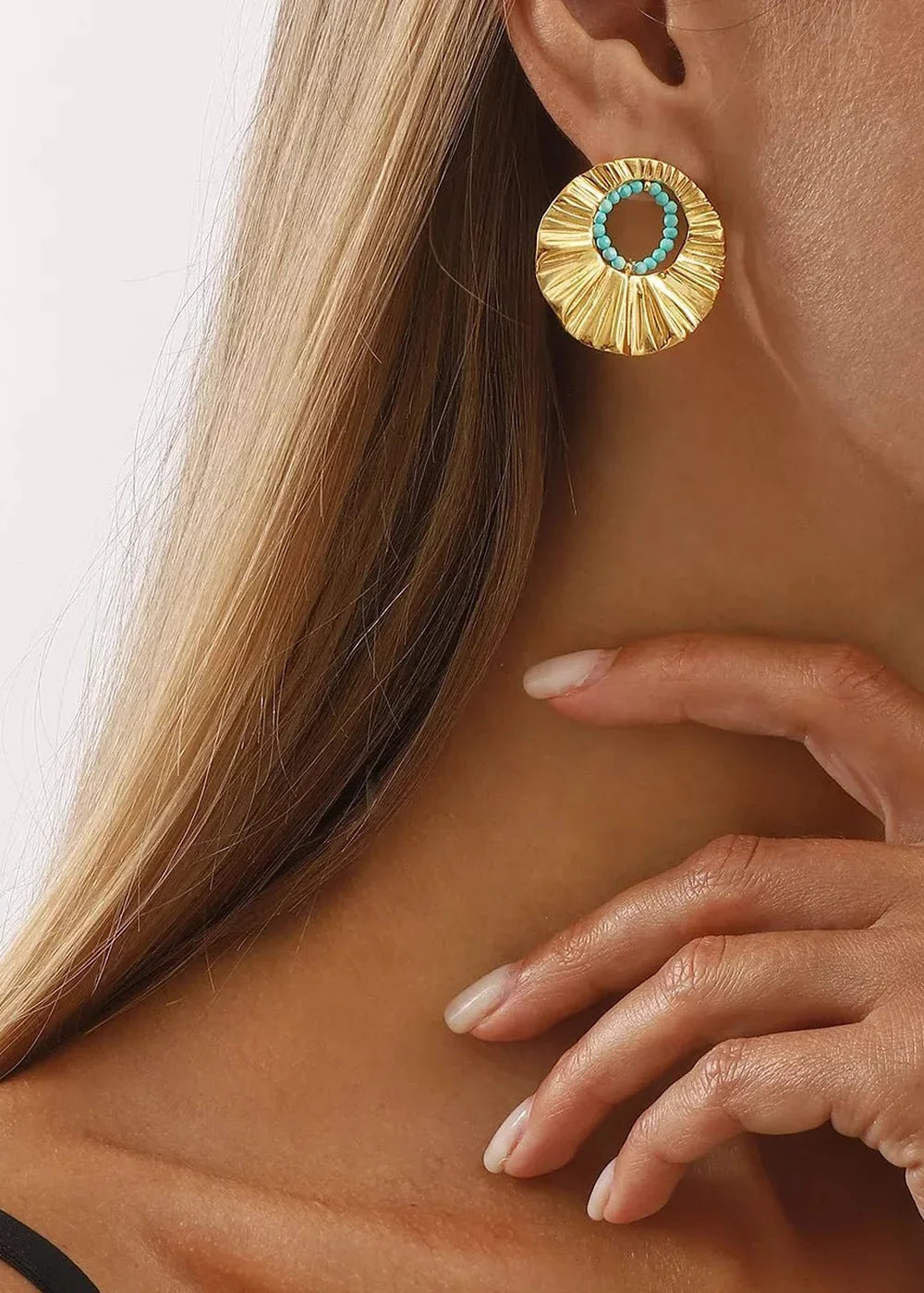 Close-up of gold-plated circular earrings with turquoise beads on a woman's ear.
