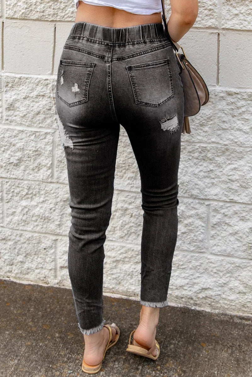 Distressed charcoal grey denim jeans with frayed hem and elastic waistband, shown from the back.
