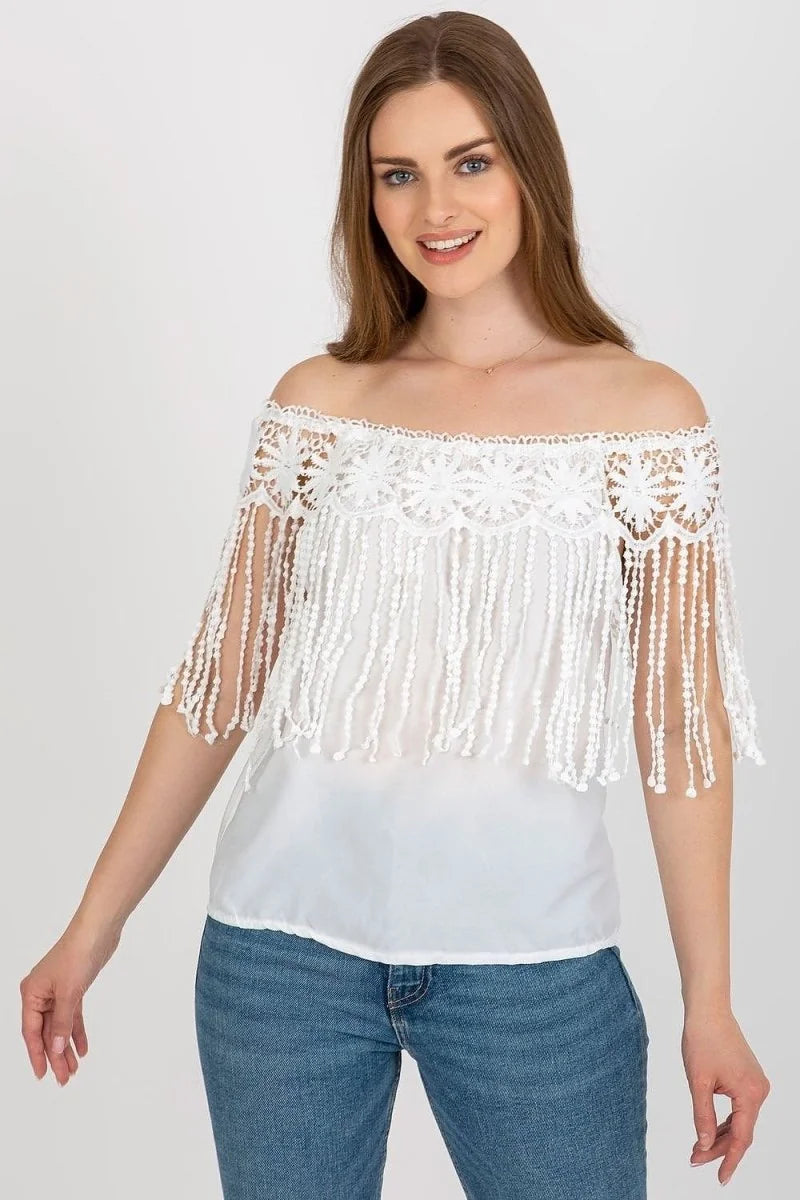 Off-the-shoulder white lace top with fringe detail and blue denim jeans on a model.