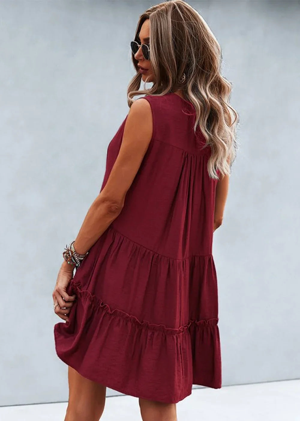 Burgundy tiered ruffle dress with sunglasses and bracelets on model, showing back view.