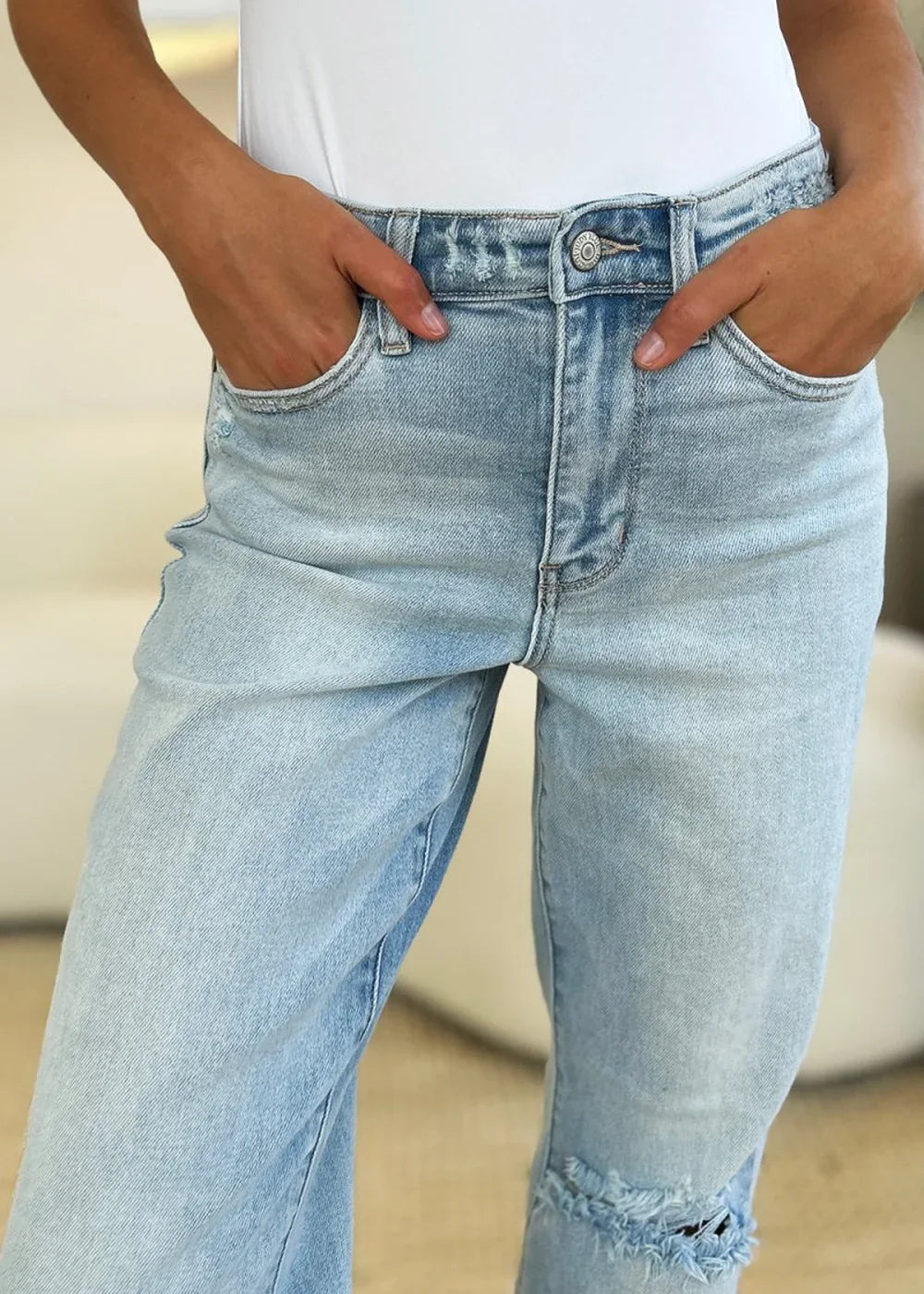 Light wash distressed denim jeans with a ripped knee detail, shown up close.