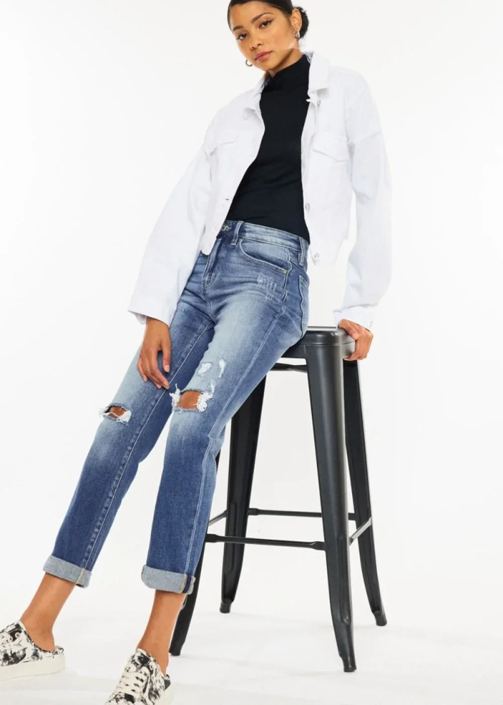 Distressed medium-wash denim jeans with ripped knees and cuffed hems, worn by a model.