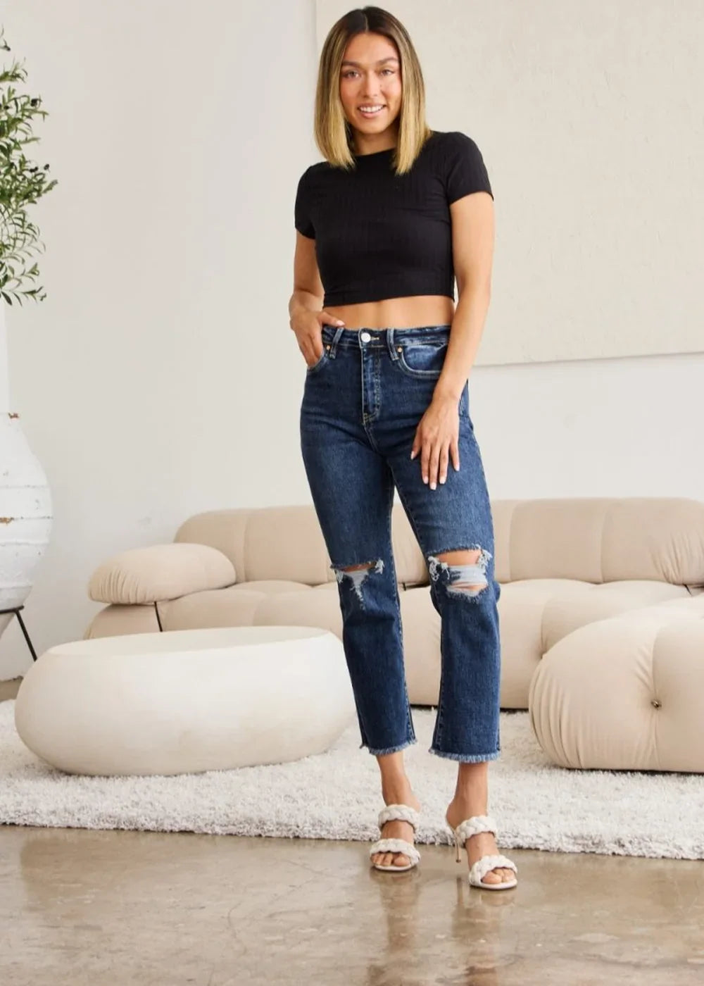 Distressed dark wash denim jeans with a frayed hem, shown on a model.