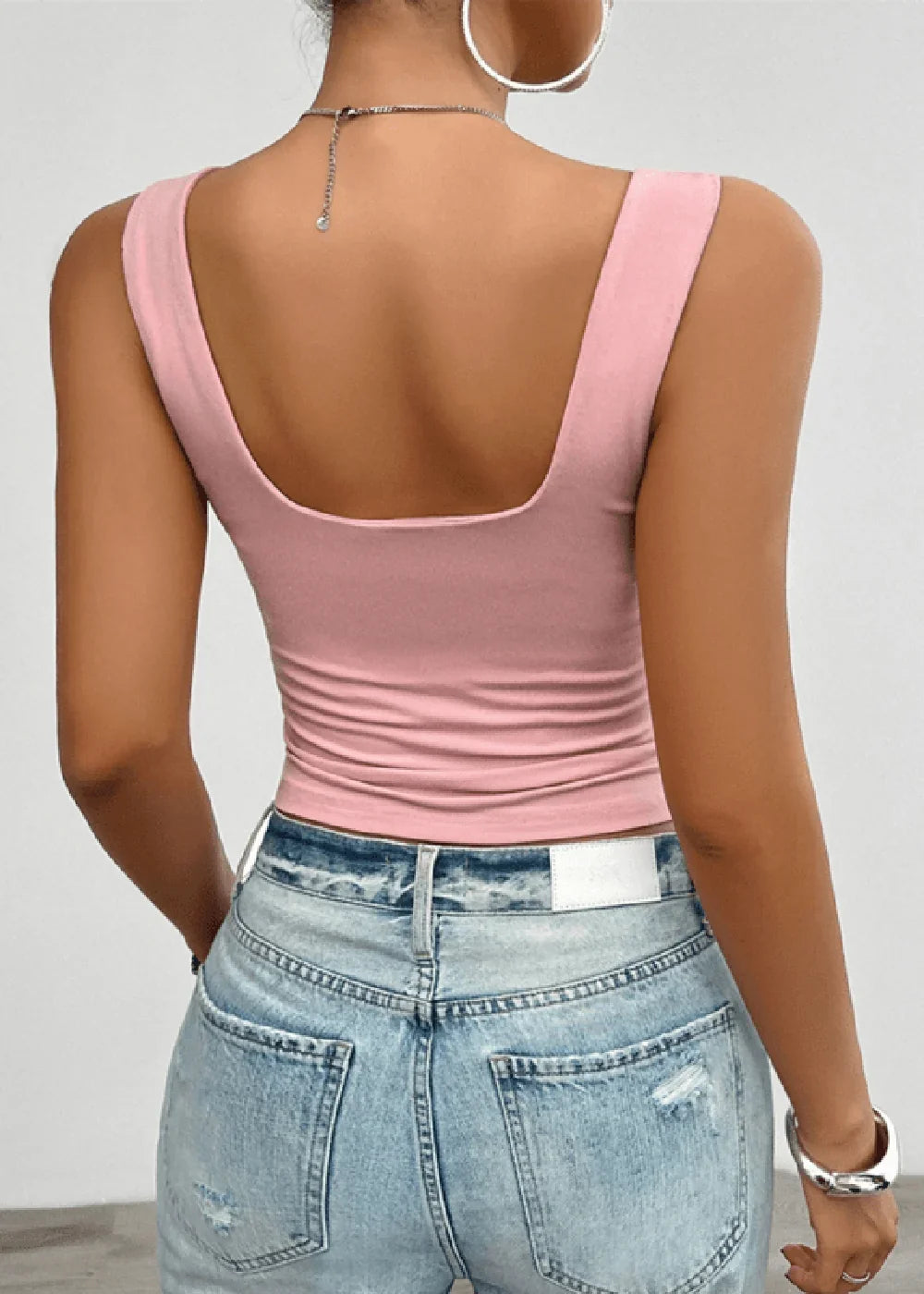 Back view of a slim-fit, light pink scoop-neck tank top on a model wearing distressed light wash denim jeans.